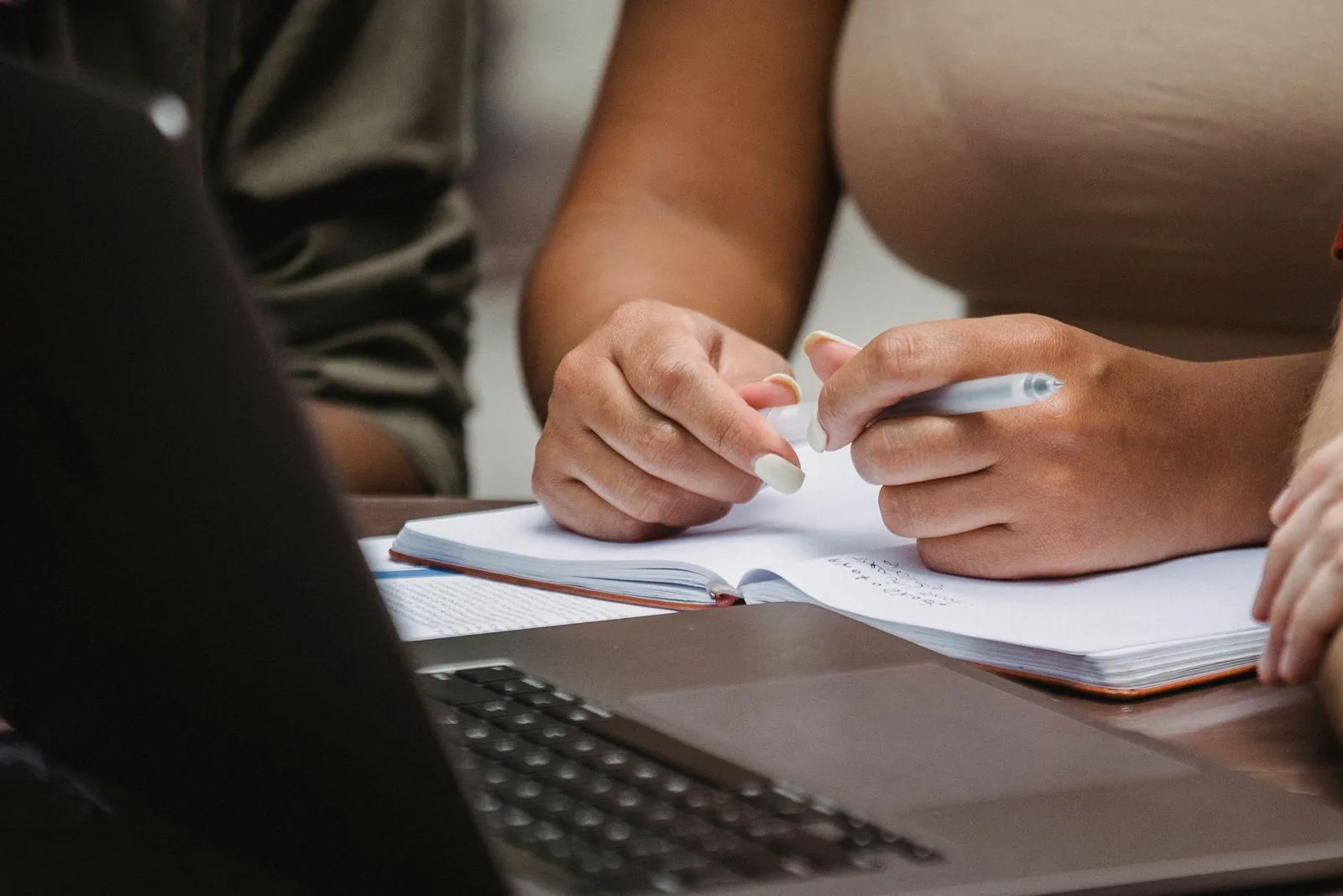 People taking notes beside a laptop during a discussion